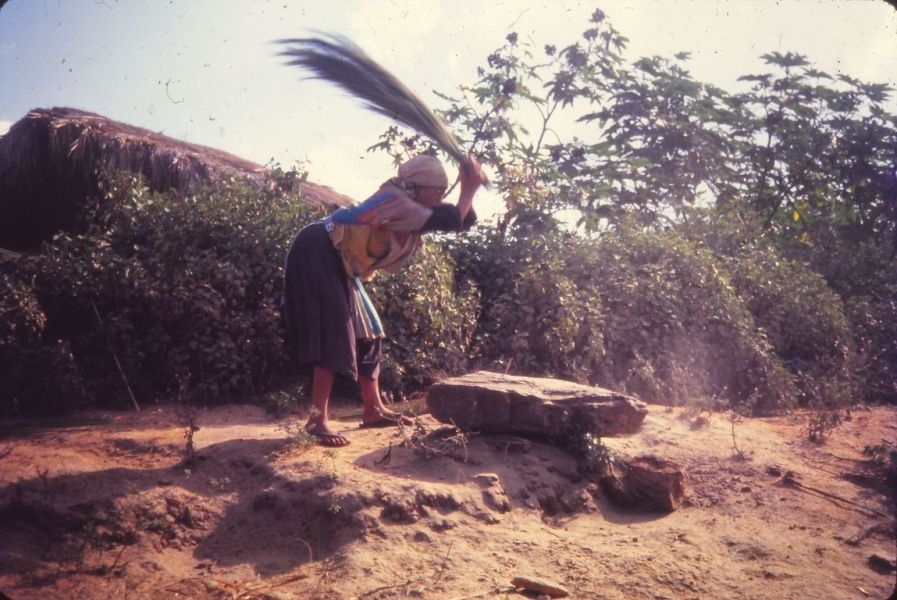 A Lisu woman is holding a bunch of grass and beat it on the big rock to remove the powder of the grass. This grass is use to make brooms. EFEO_KLEO00191
